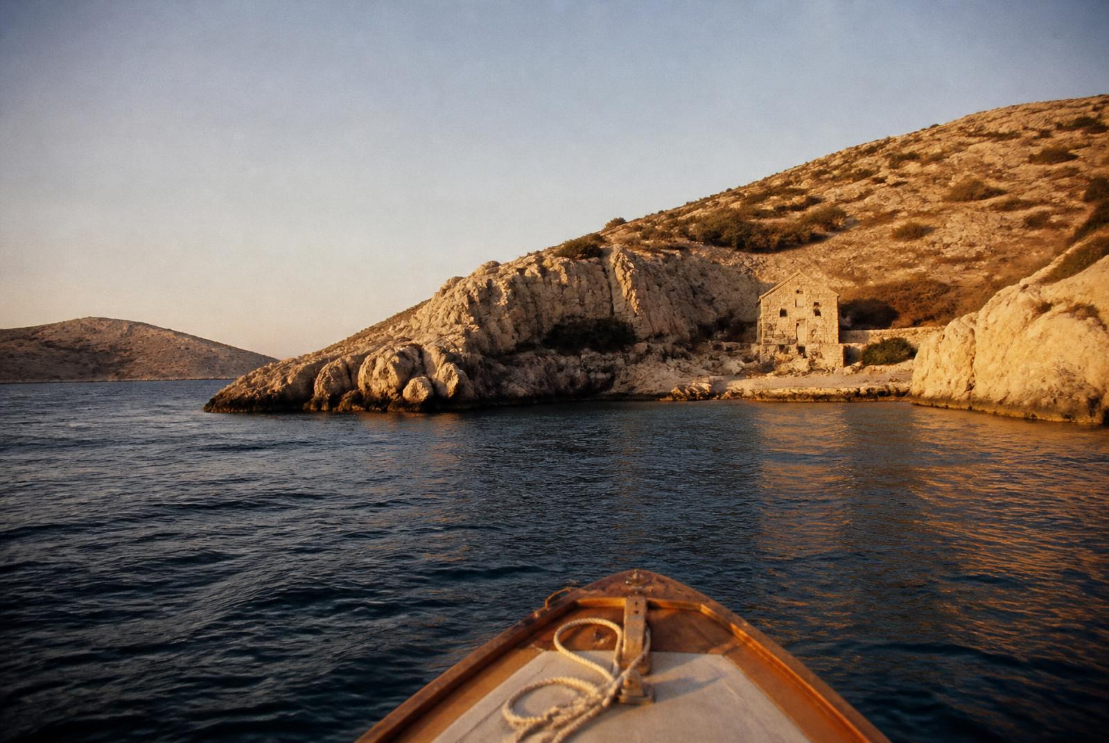 A wooden boat approaching a stone house in a remote Kornati cove at golden hour
